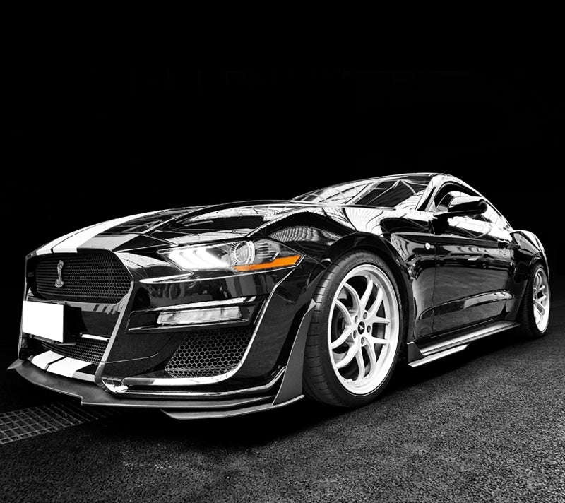 Low-angle front view of a black 2018–2022 Ford Mustang featuring a Shelby GT500 front bumper conversion, highlighting the aggressive stance, aerodynamic front splitter, and white racing stripes.