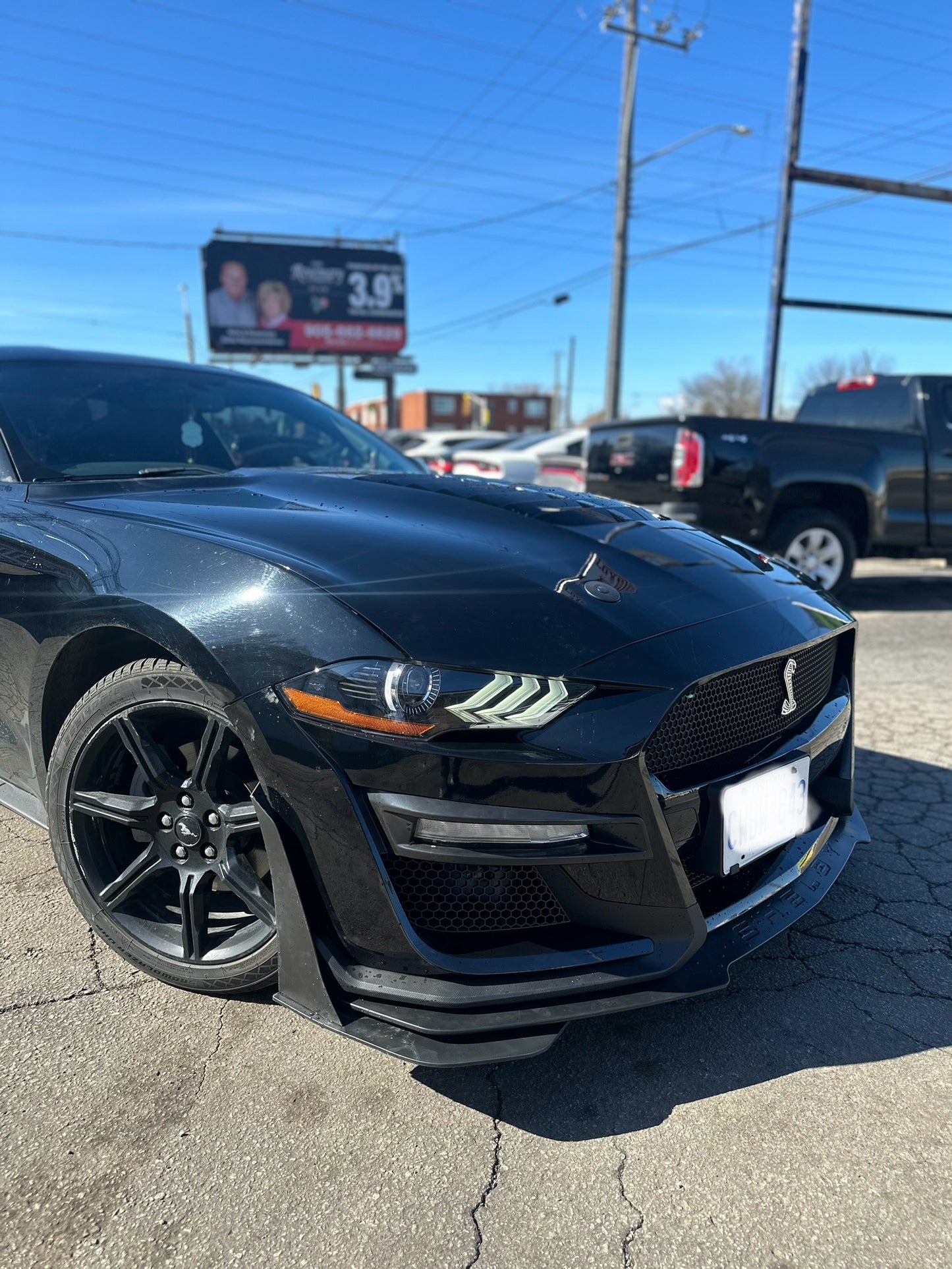 Close-up of a black 2018–2022 Ford Mustang featuring a Shelby GT500 front bumper conversion kit, highlighting the sleek design, modern headlights, and aerodynamic splitter.