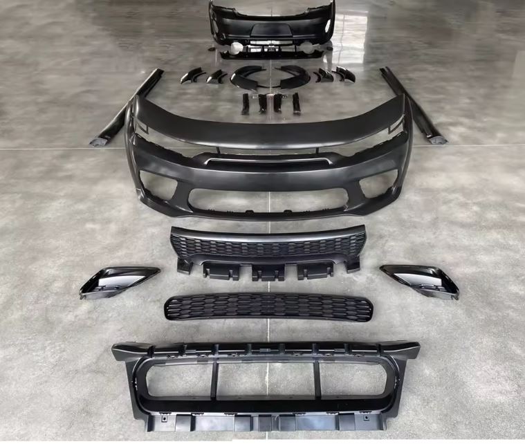 Complete Dodge Charger Hellcat-style wide body kit laid out on a smooth concrete floor, showing front bumper, rear bumper, grilles, fender flares, and side skirts — available from OneCarWorld.