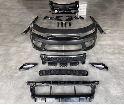 Complete Dodge Charger Hellcat-style wide body kit laid out on a smooth concrete floor, showing front bumper, rear bumper, grilles, fender flares, and side skirts — available from OneCarWorld.